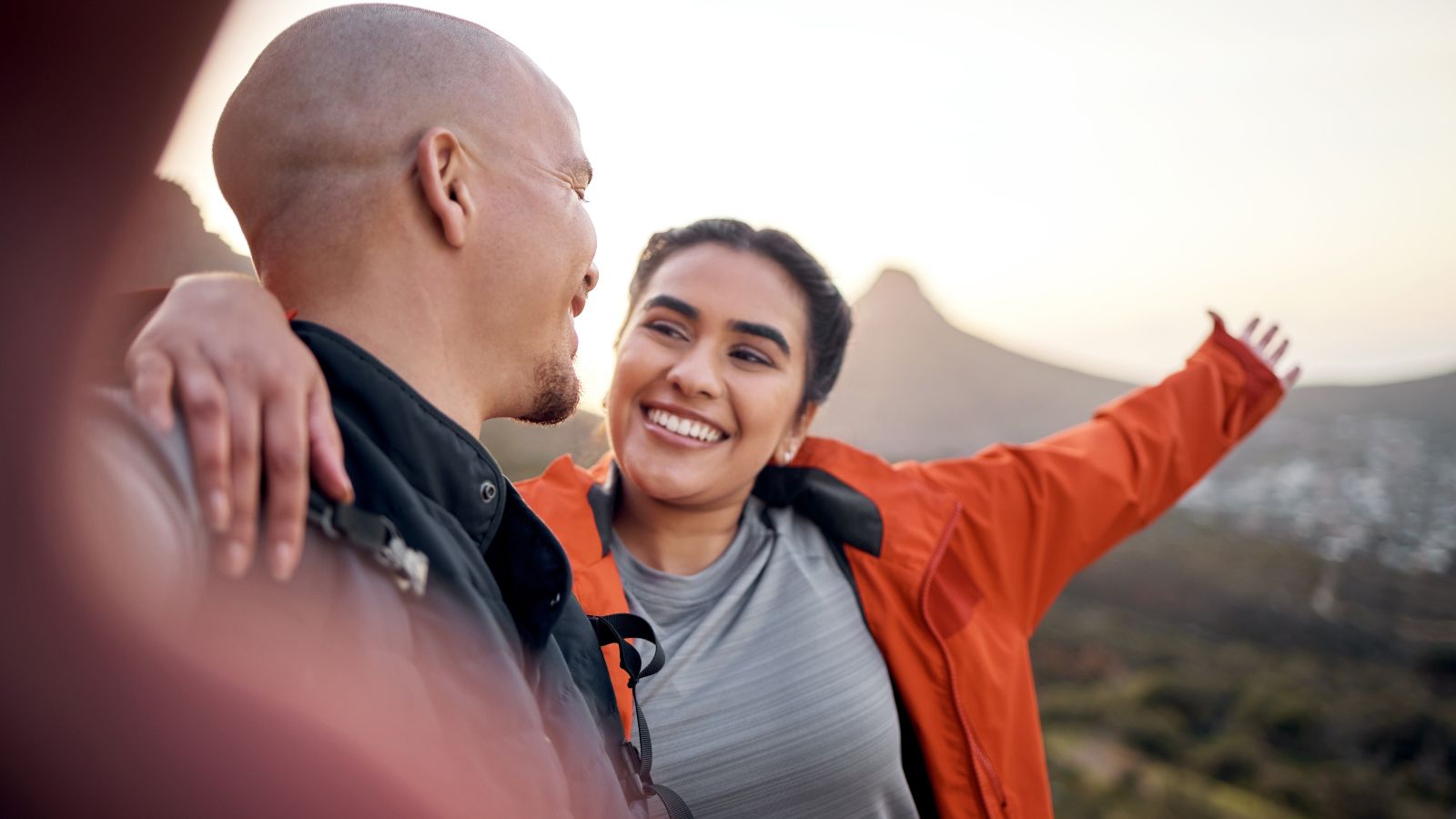 A photo of a Couple celebrating at a scenic summit overlook, smiling and standing close together.