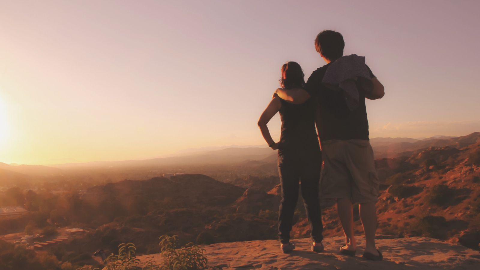 A photo of a Couple standing together at a red rock overlook in Sedona at sunrise.