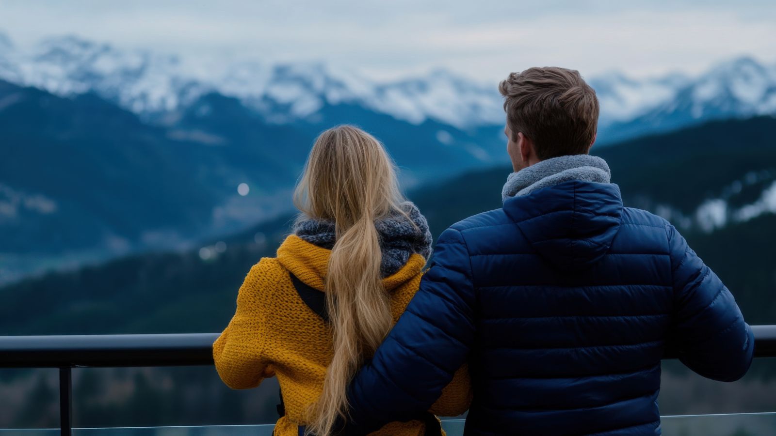 A photo of Couple standing close together overlooking snowy mountain scenery and a quiet river.