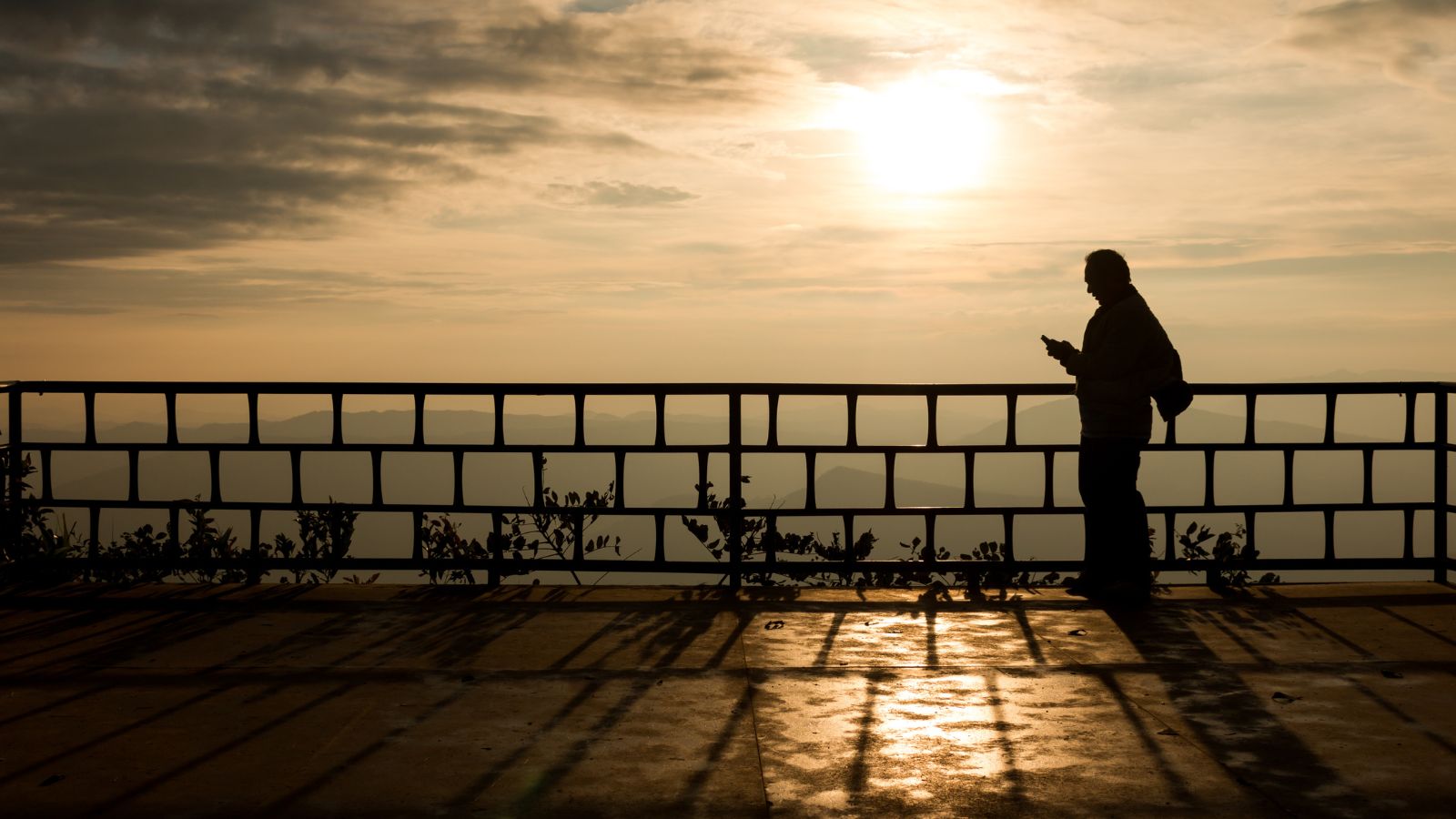 A photo of a Person standing quietly at sunrise on a balcony overlooking a city.