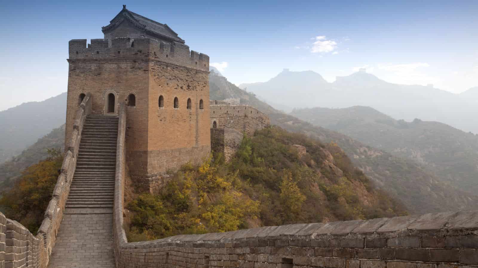 The Great Wall of China winds past a watchtower and stone steps with mountains in the background.
