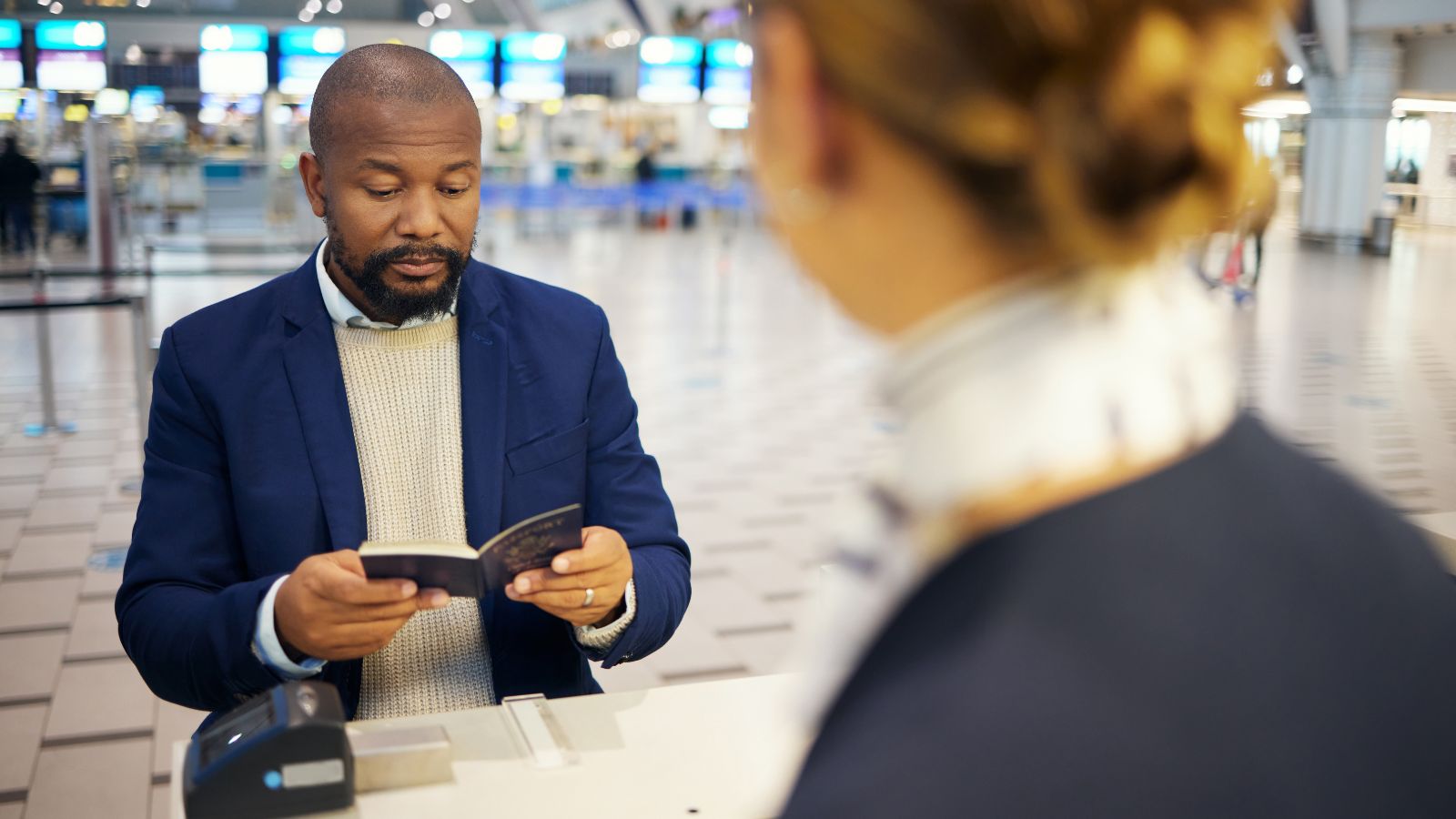 A photo of an Immigration officer speaking with traveler at passport control desk.