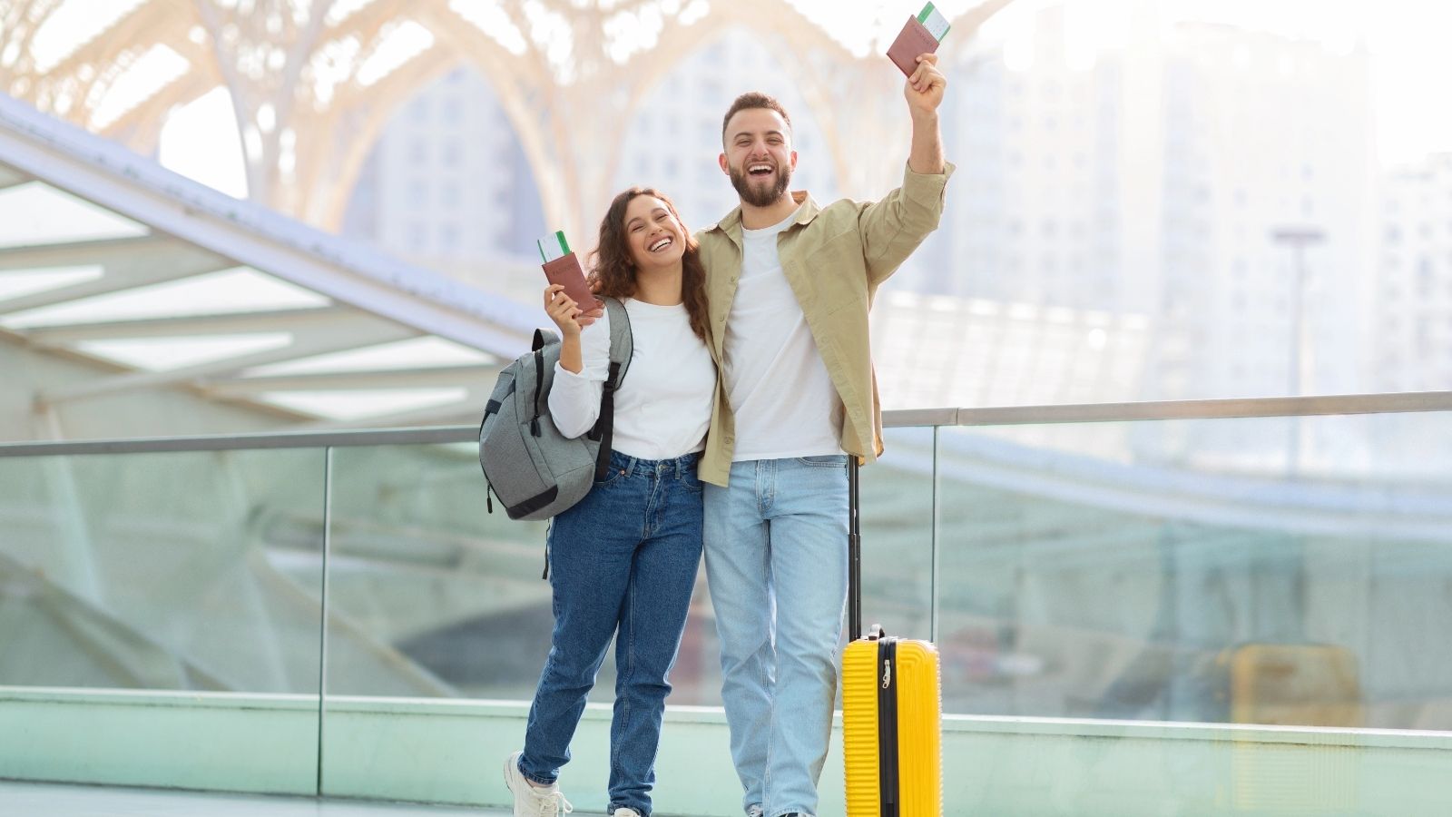 An image of a couple smiling and holding their passports up at the airport.