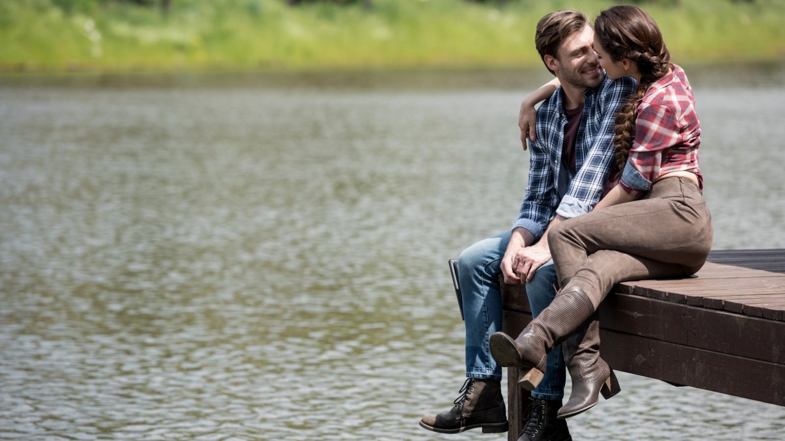 A couple sitting by the dock by a lake.