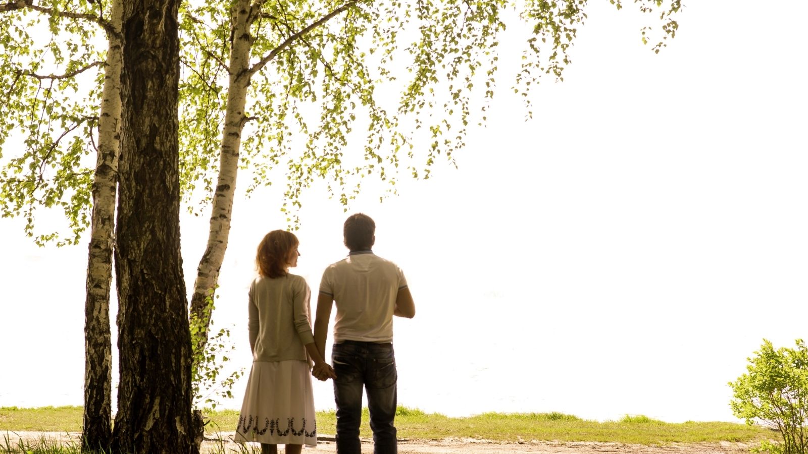 An image of a couple holding hunds under a birch tree.