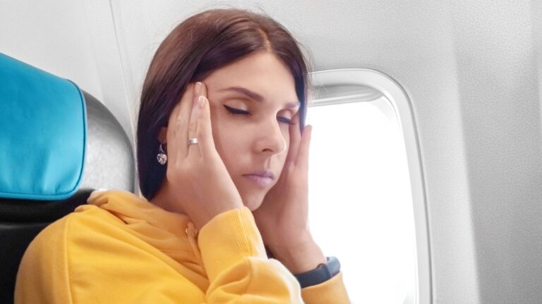 An image of a girl massaging her temples on the plane.