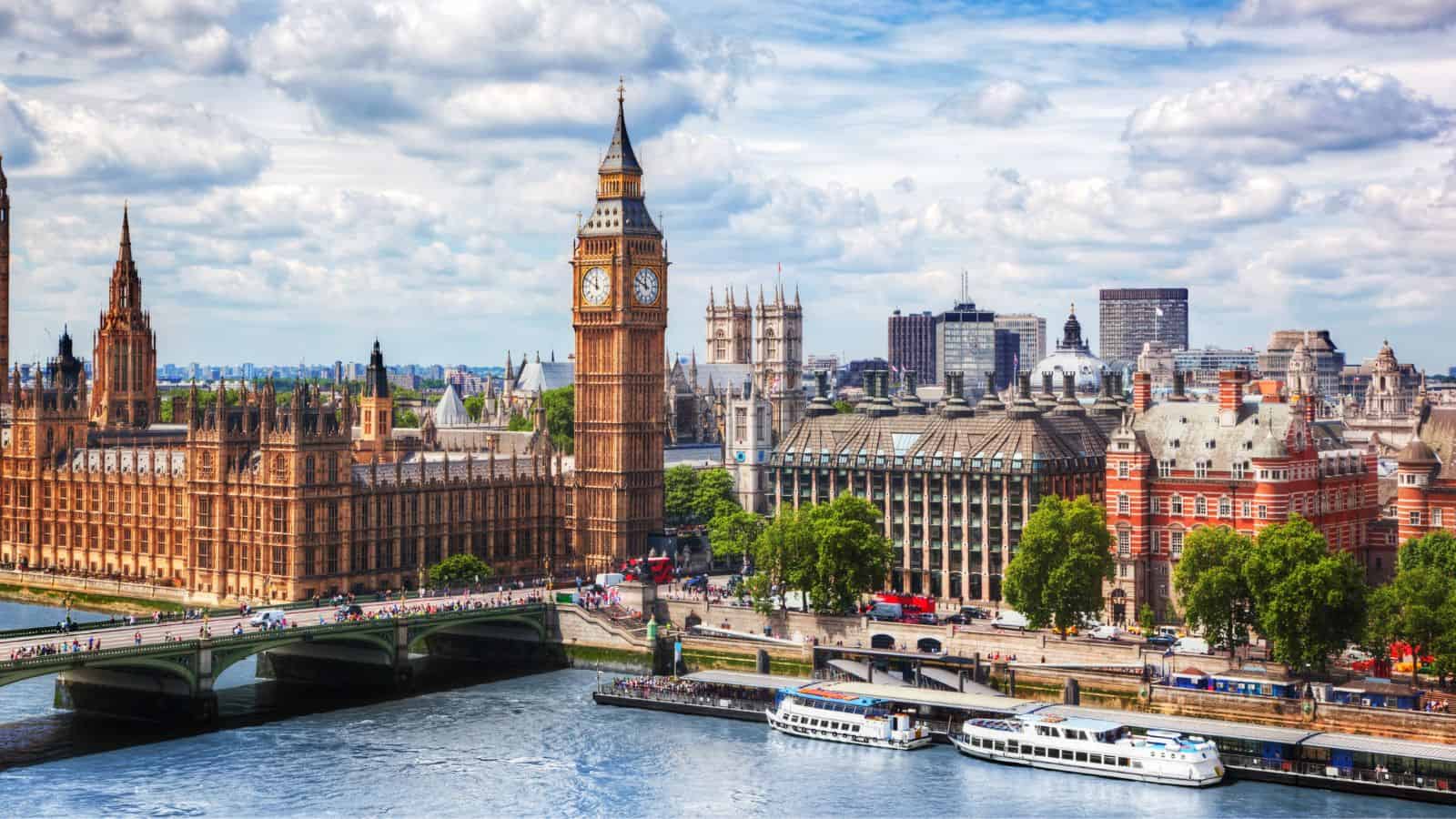 A must-visit view of London features the River Thames, the iconic Houses of Parliament, and Big Ben. Two boats drift along as vehicles cross Westminster Bridge. The partly cloudy sky frames a cityscape rich with diverse architecture and greenery, promising endless museums and art to explore.