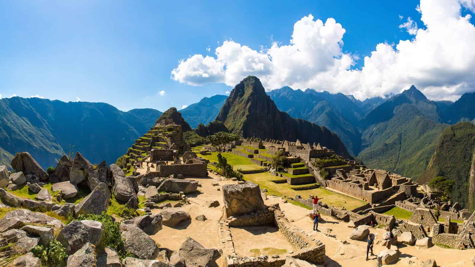 Machu Picchu ruins in Peru amid green mountains under a blue sky with clouds.