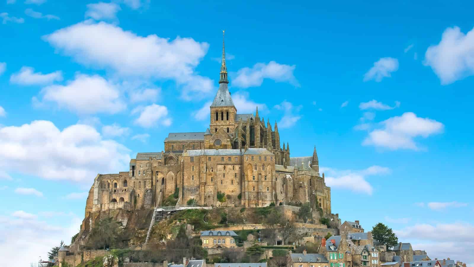Mont Saint-Michel, a fortified abbey village, stands on a rocky island beneath a blue sky with scattered clouds.