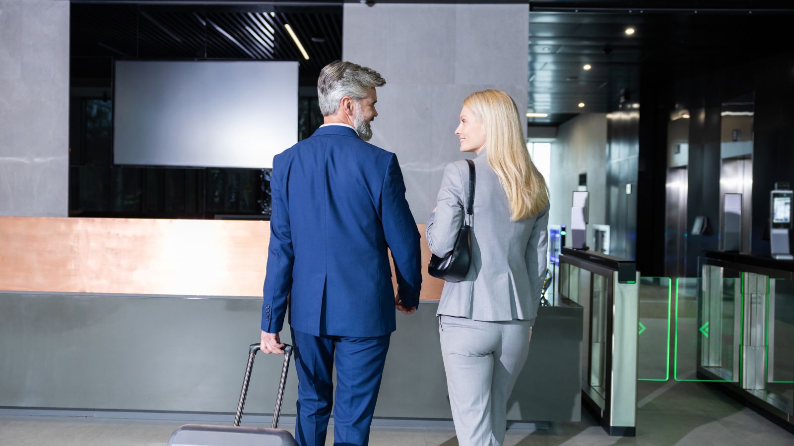 A photo of a two aged couple, entering a hotel with luggage and formal suit.
