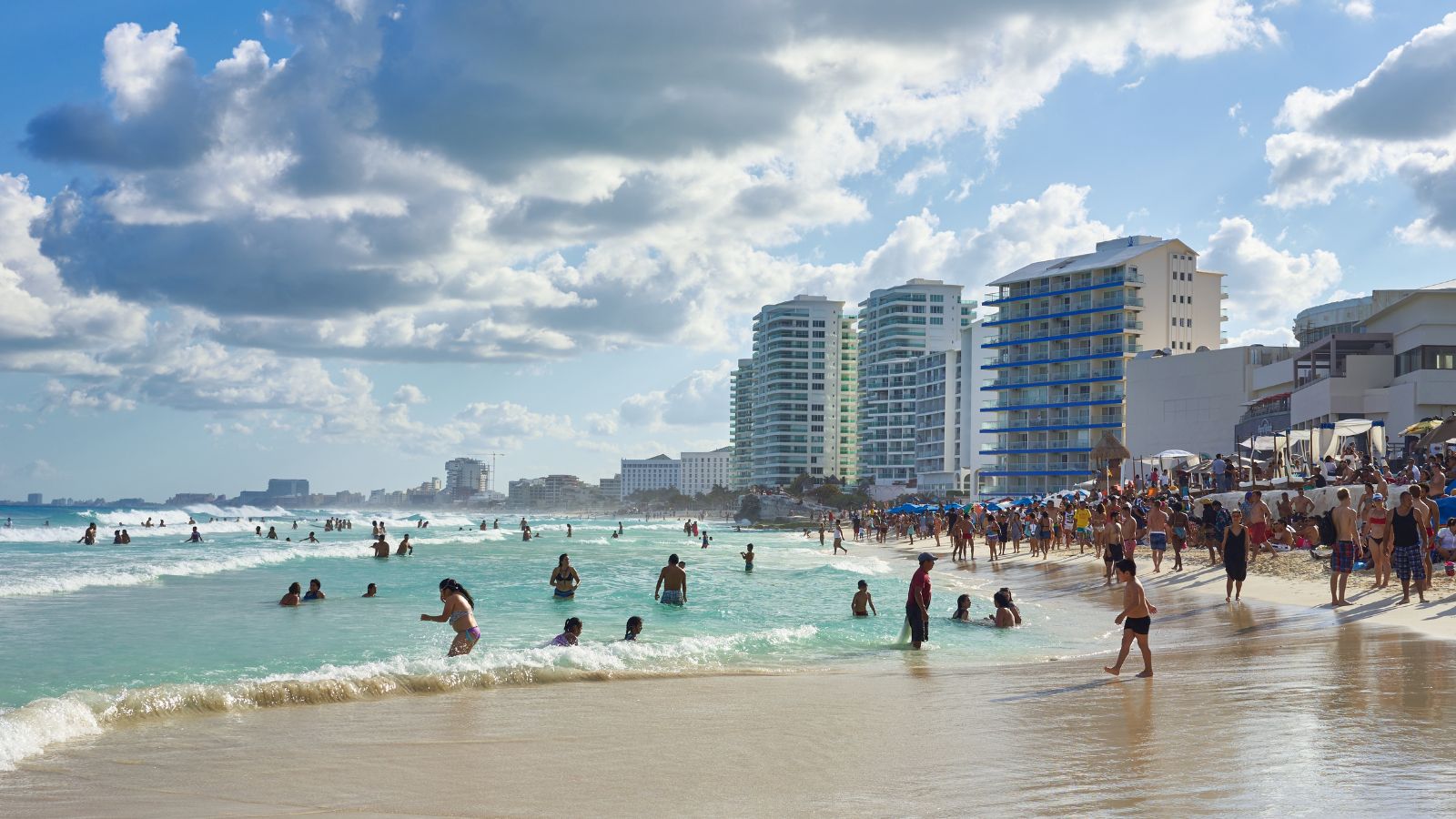 A photo of a Wide Cancun beach with calm turquoise water, people swimming and floating near shore.