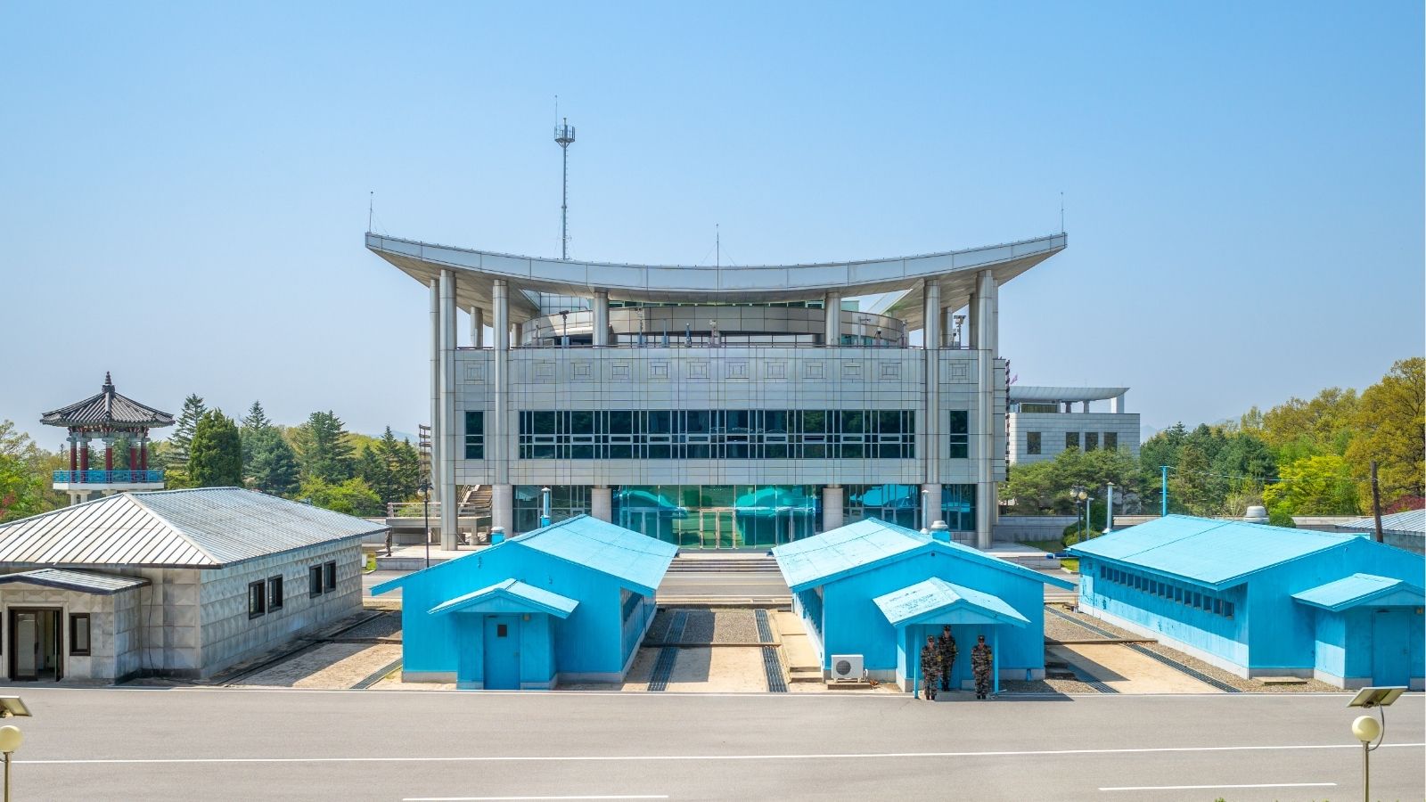 Joint Security Area at the Korean DMZ with blue conference buildings and a large modern building in the background.