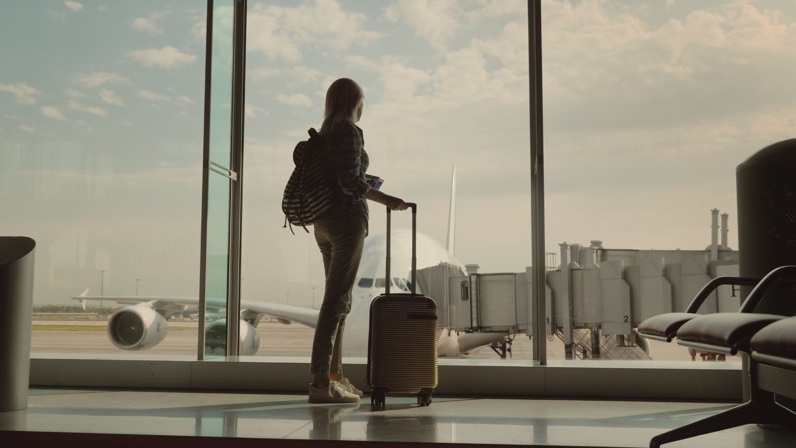 A photo of a woman, holding a luggage looking up in the sky inside airport.