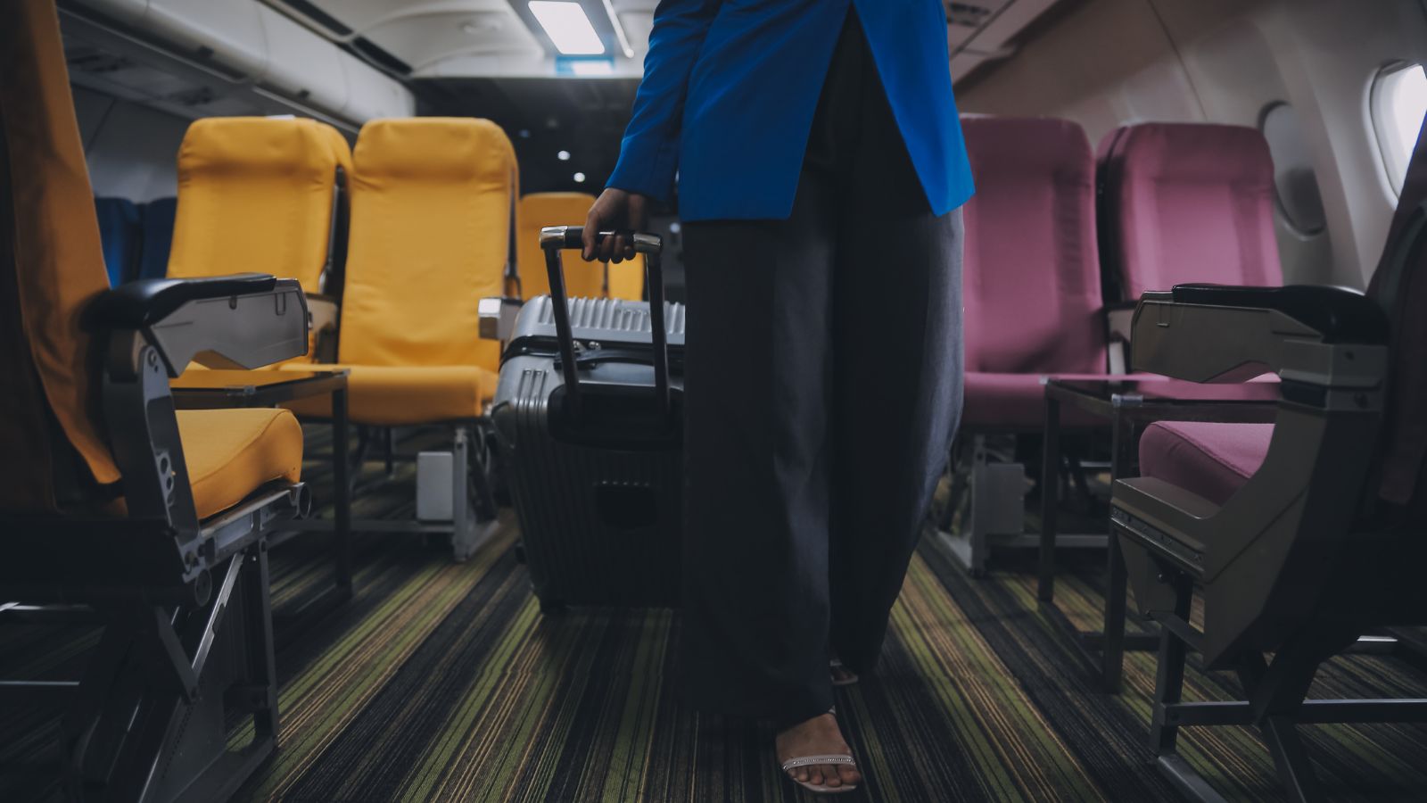 A photo of a woman walking inside a plane carrying a luggage.