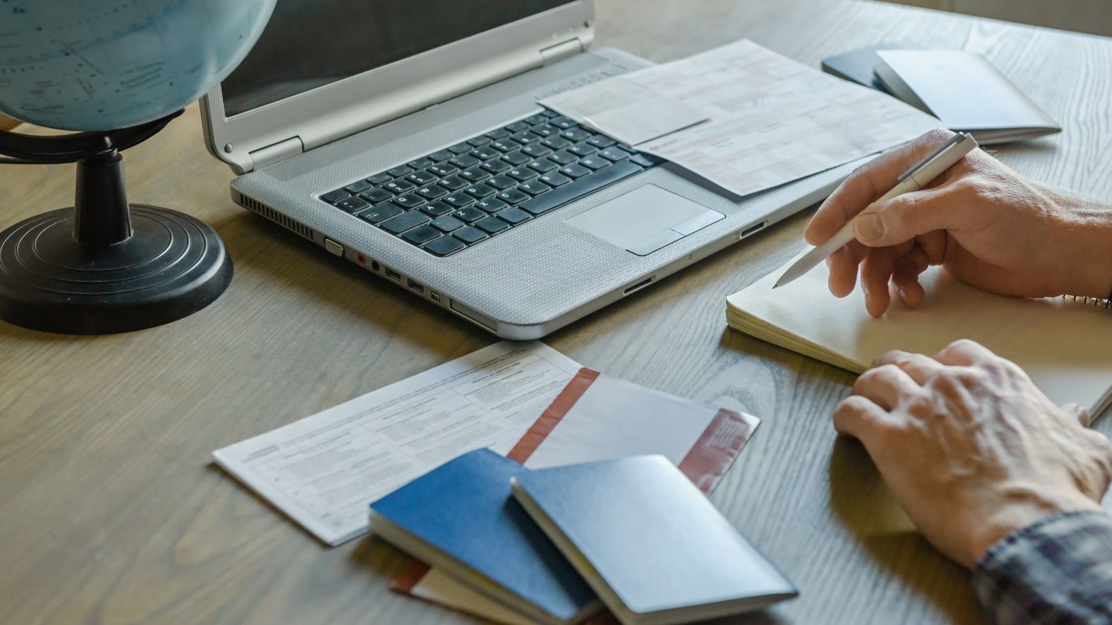 A photo of a man with open laptop and notebook with maps and notes.