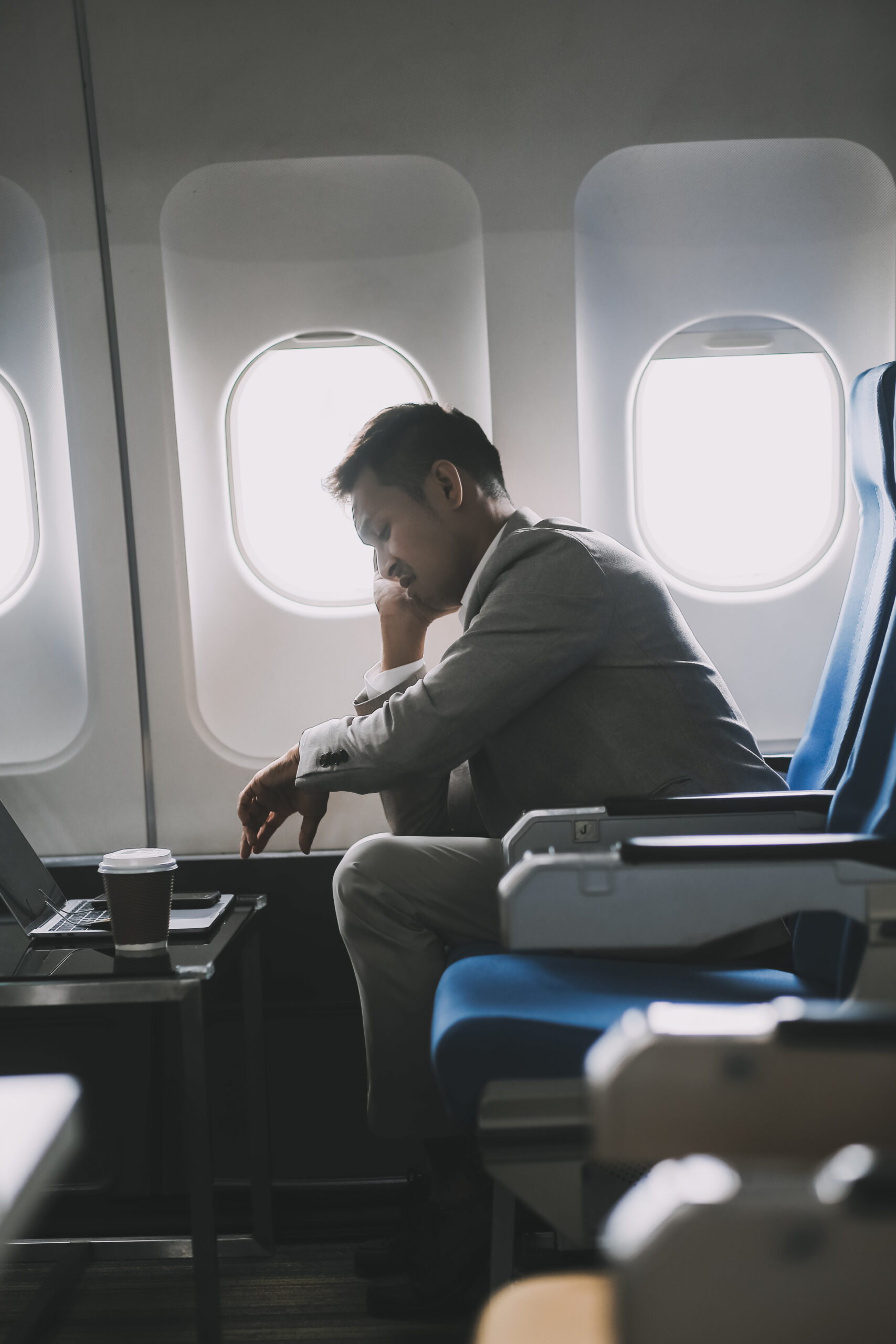 tressed and professional Asian businessman in a business class, having a serious phone call with someone during the flight to a business meeting.