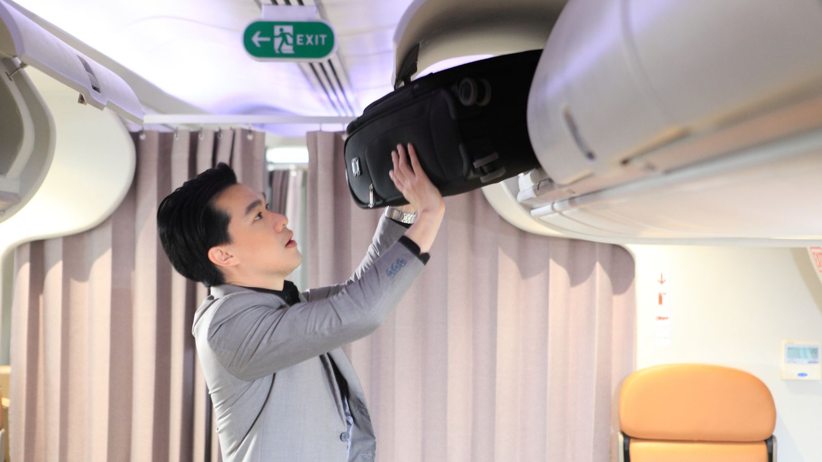 A photo of a passenger placing carry on overhead bin airplane aisle.
