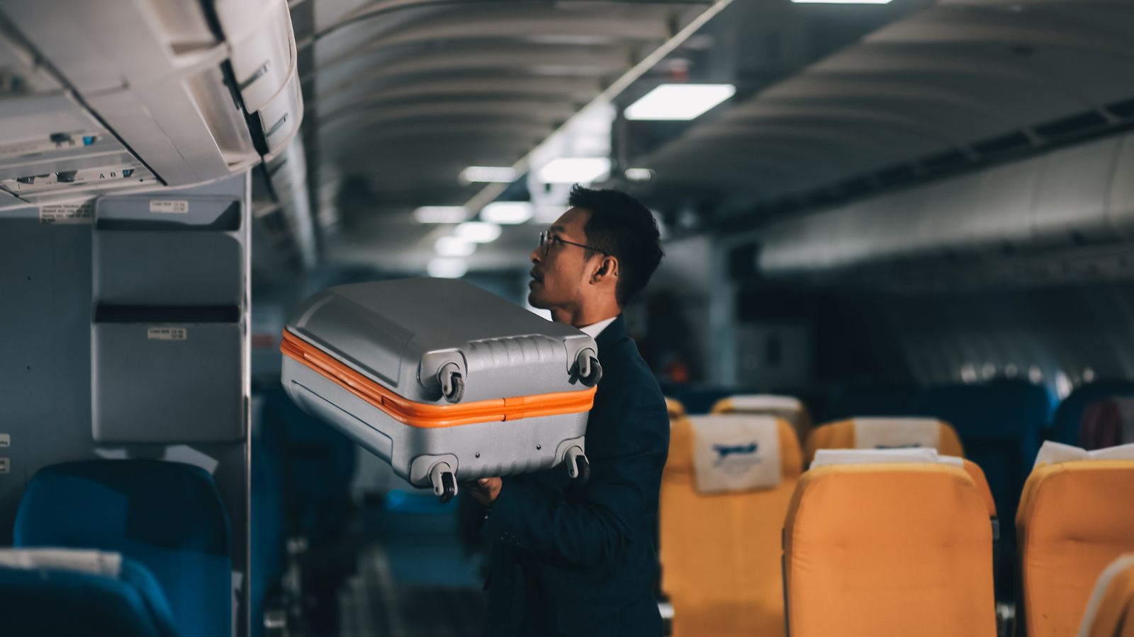 A photo of a passenger organizing carry on luggage quickly inside airplane aisle.