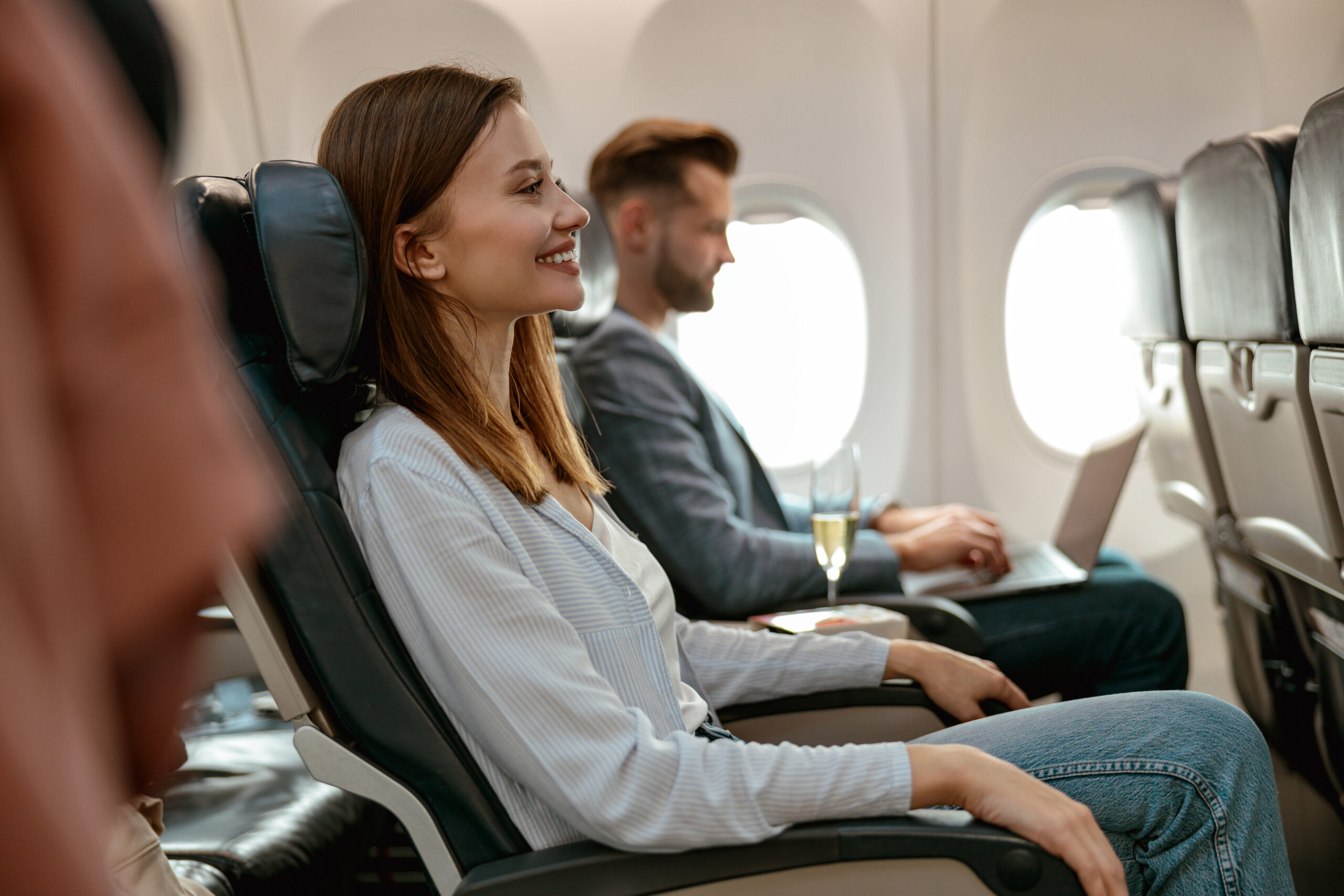 Joyful female person sitting in passenger seat next to man and smiling while traveling by plane.