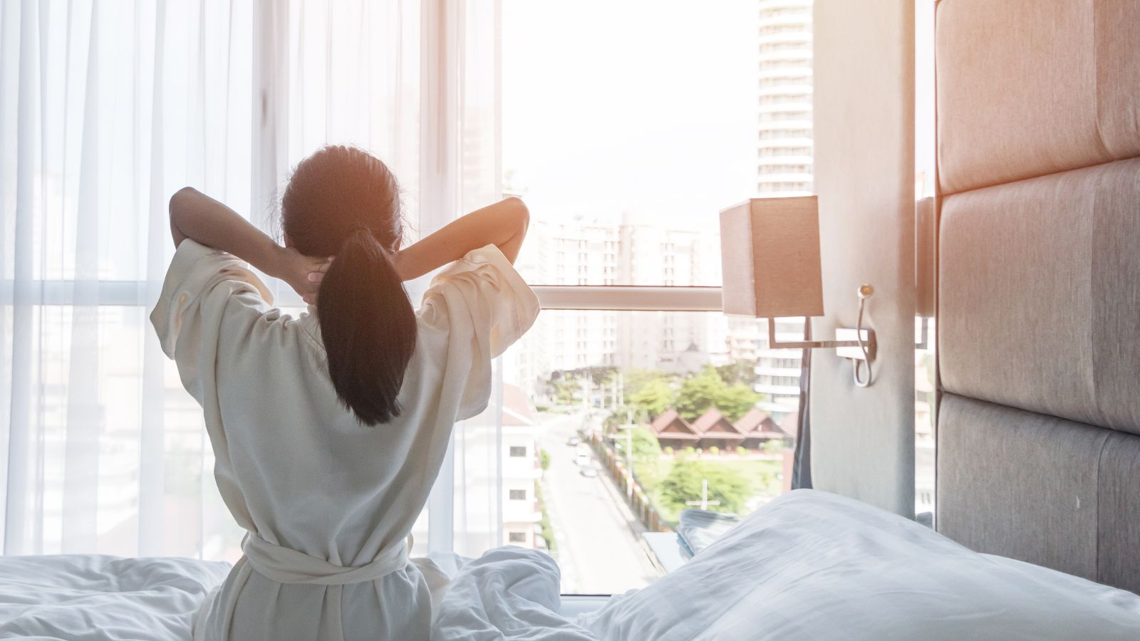 A photo of sunlit hotel room, cozy bed, morning tranquility, relaxed traveler enjoying the view.