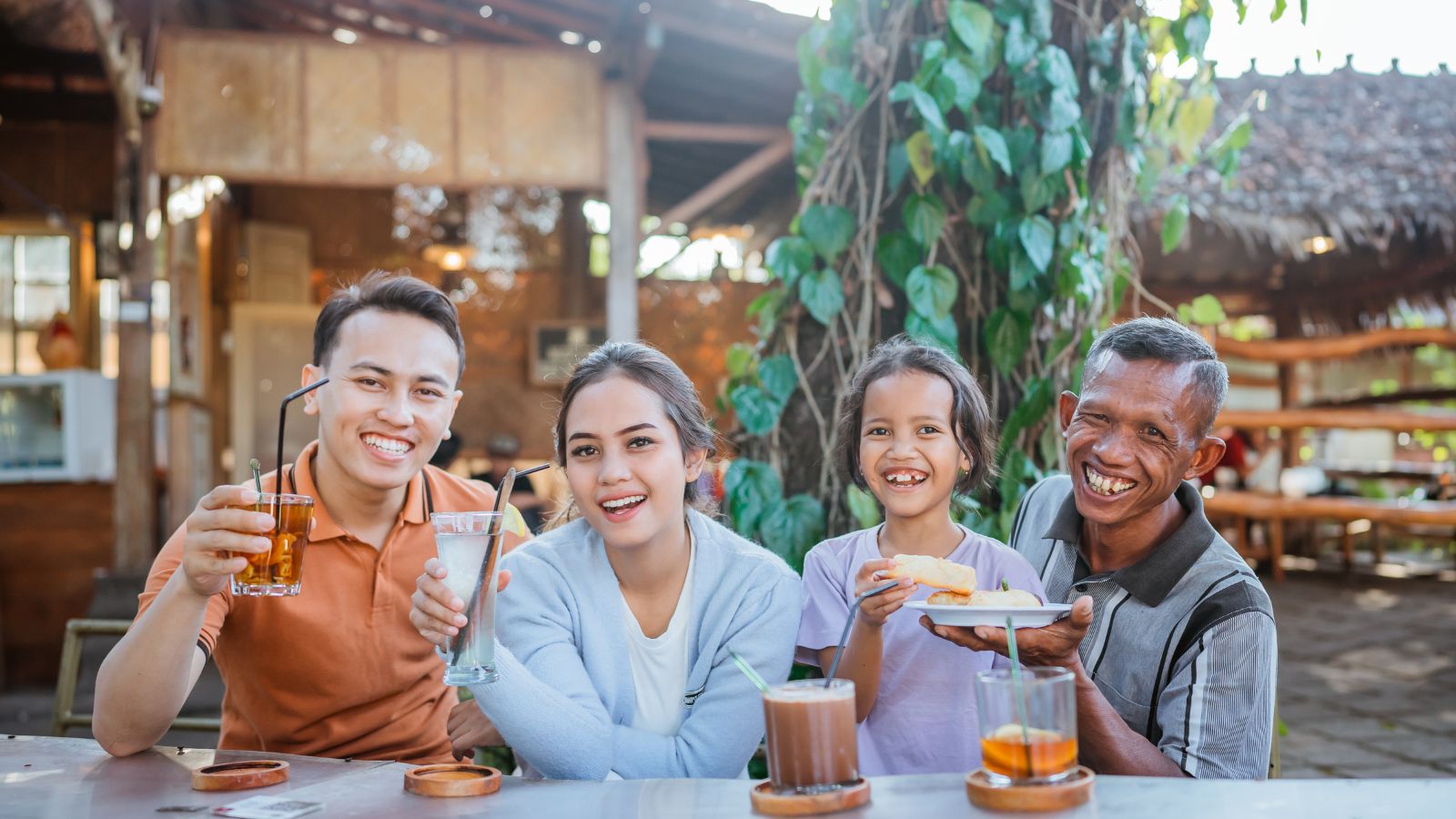 A photo of a Traveler enjoying meal calmly, sipping water or cooling drink, relaxed smile, shared table with locals, warm atmosphere, appreciation of local food culture.