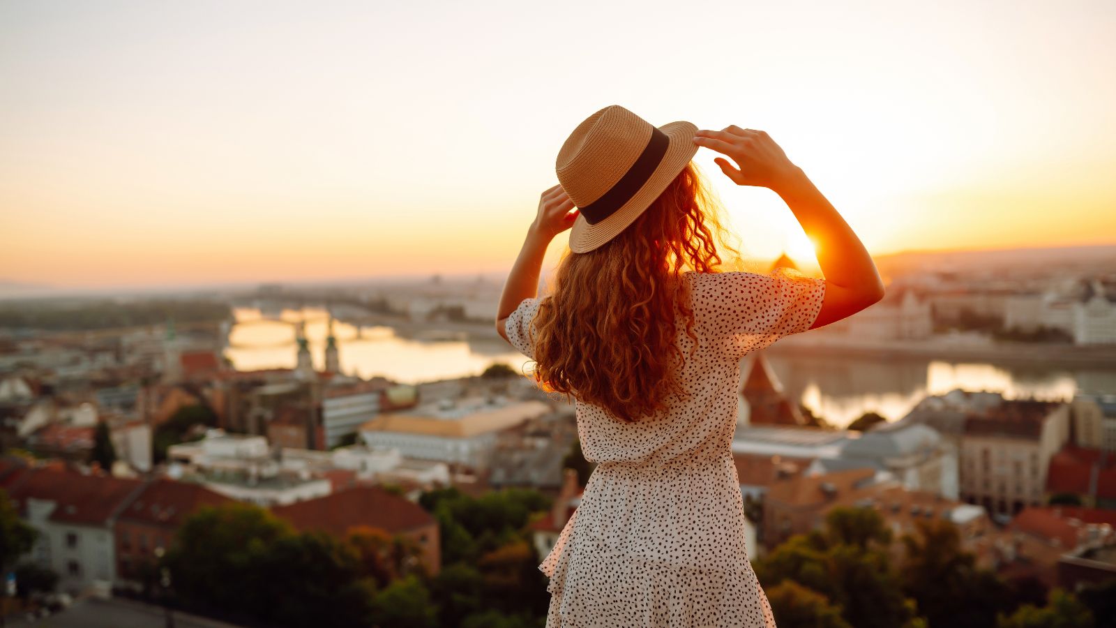 A photo of a woman facing city view during sunset.