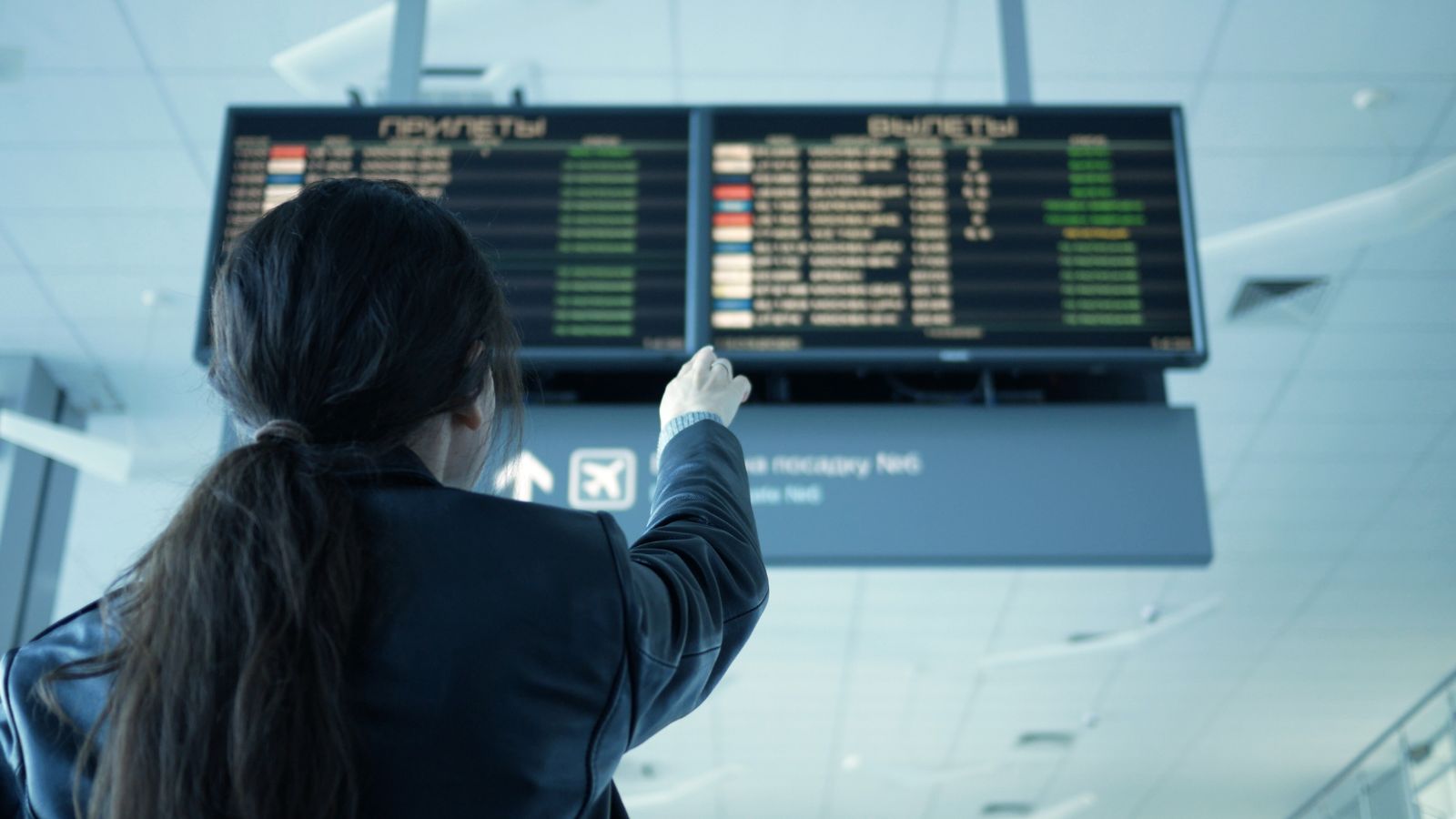 A photo of a woman in the airport pointing at the board screen.