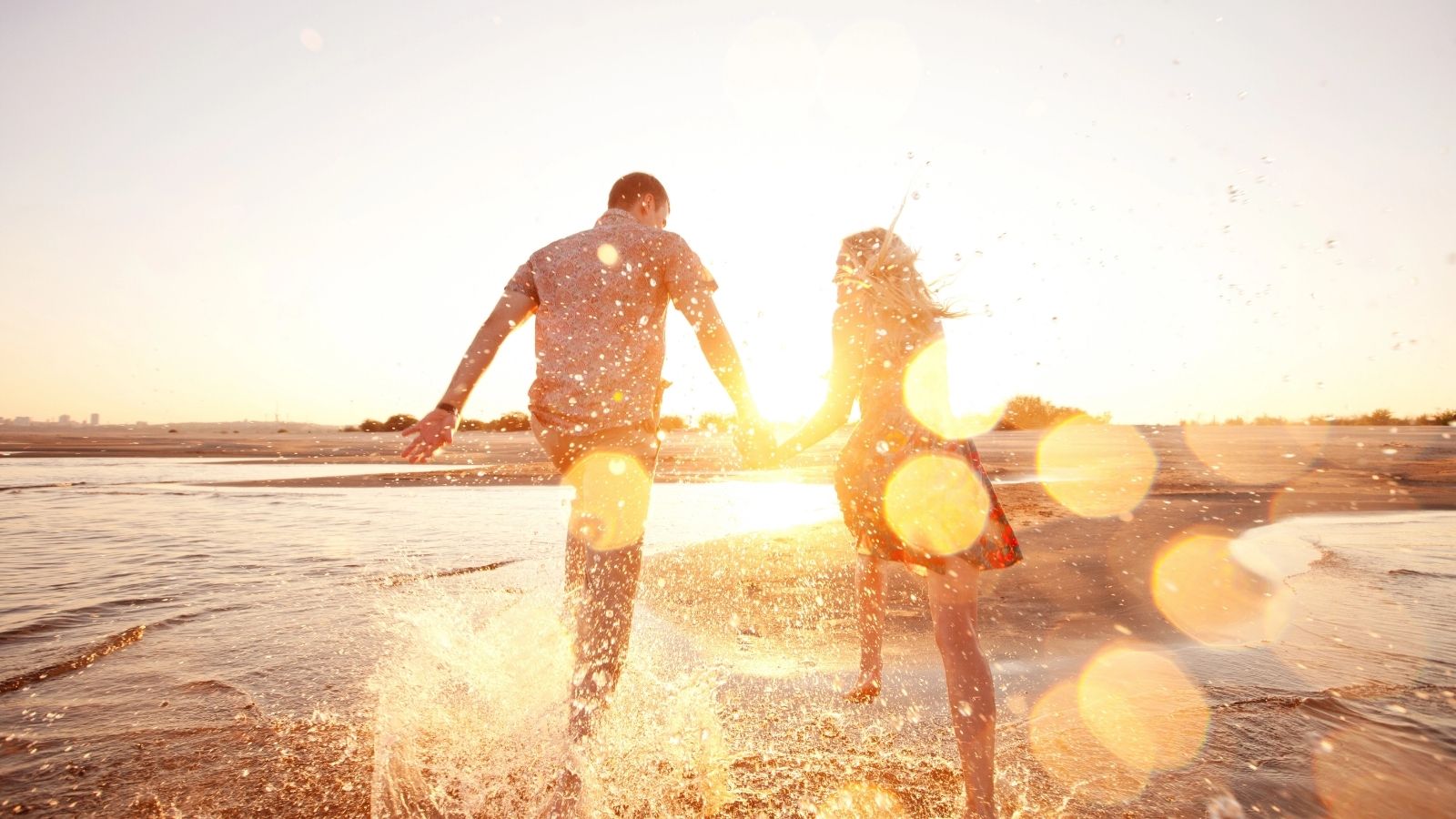 A couple holding hands walking towards the water at the beach.