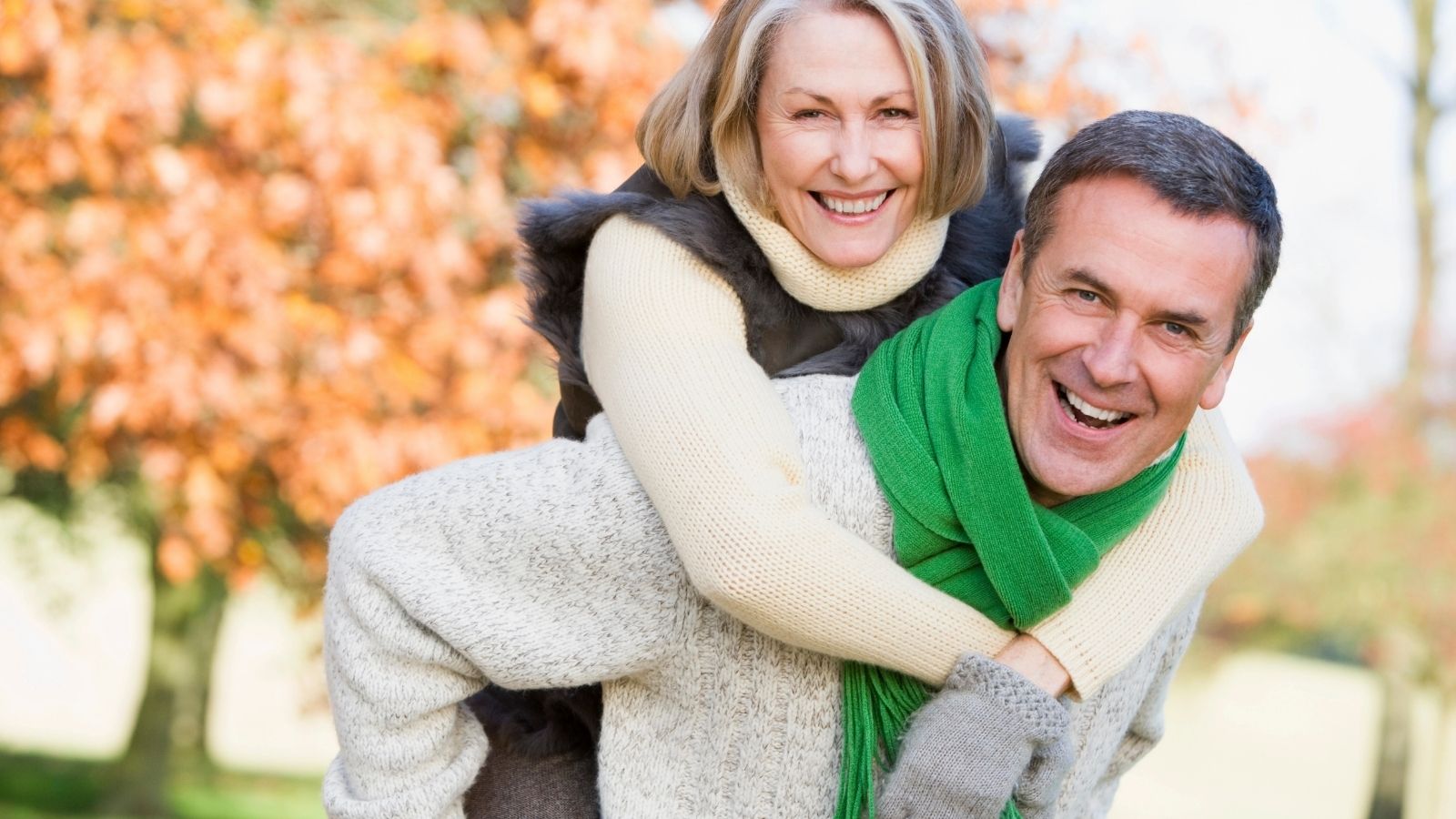 An image of a couple where the man is piggybacking the woman at a park.