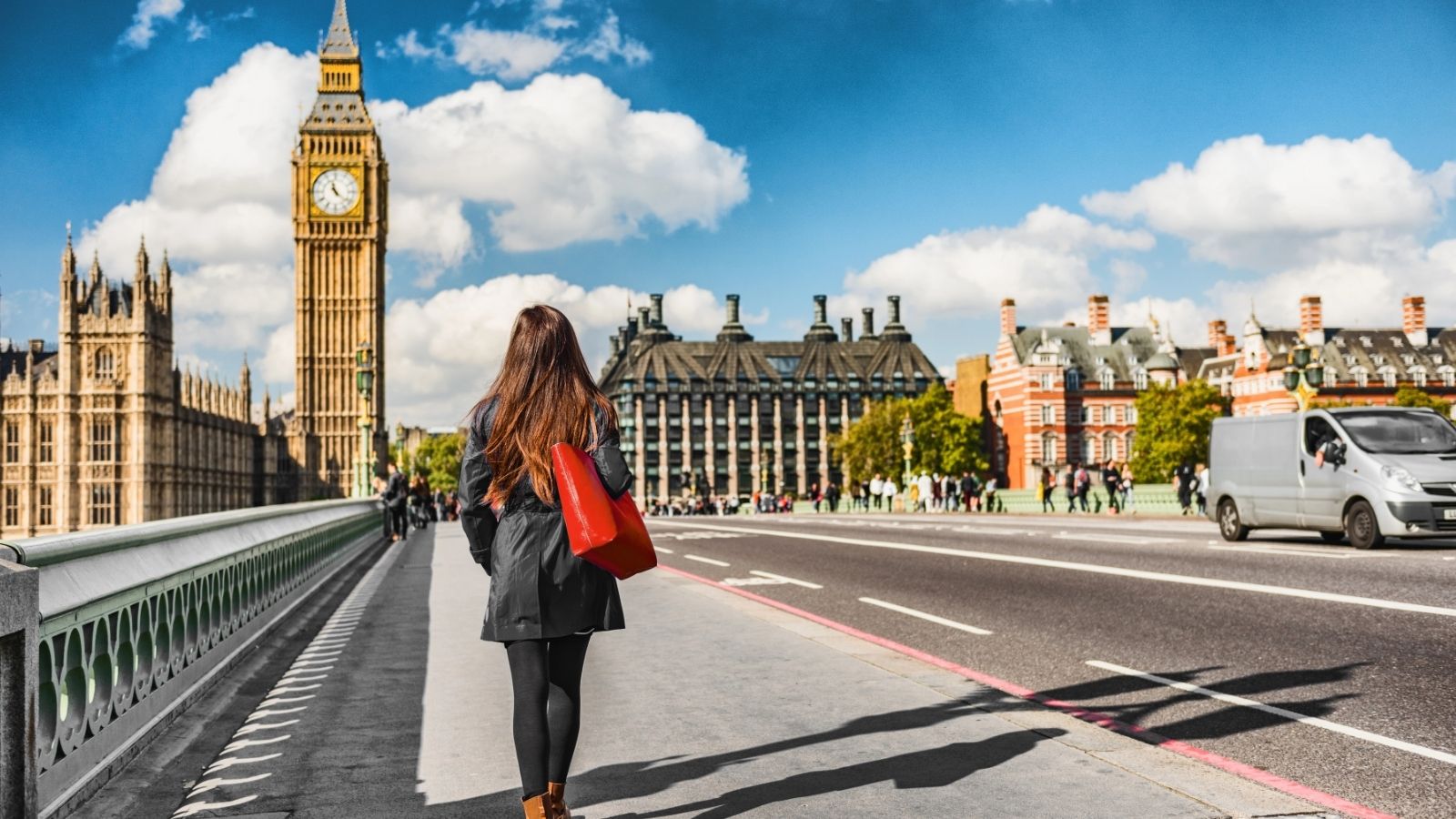 A woman carrying a red bag walks on Westminster Bridge in London with Big Ben and Parliament under a blue sky.