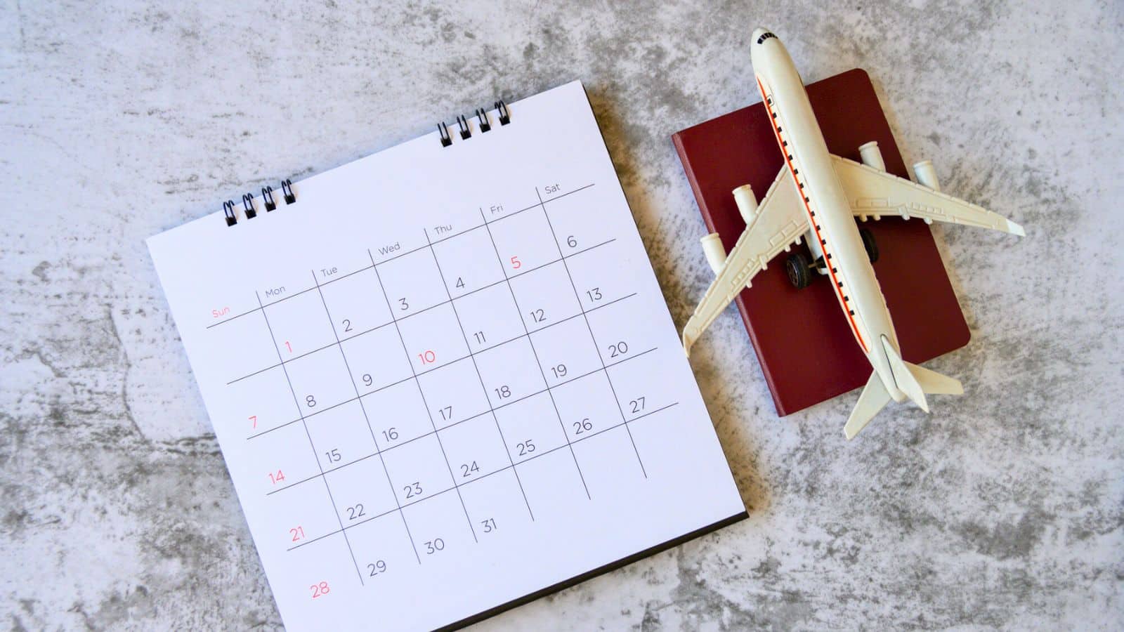 An open calendar, toy airplane, and passport rest on a gray tabletop.
