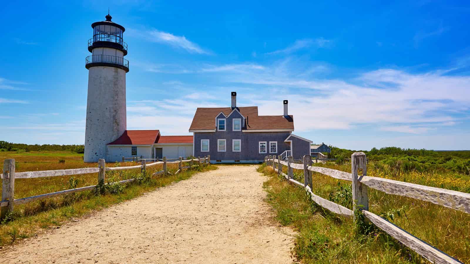 A hand puts a coin in a pink piggy bank on a suitcase, with sandy beach and ocean in the background.