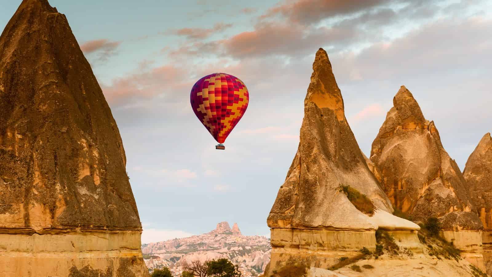 A hand puts a coin in a pink piggy bank on a suitcase, with sandy beach and ocean in the background.
