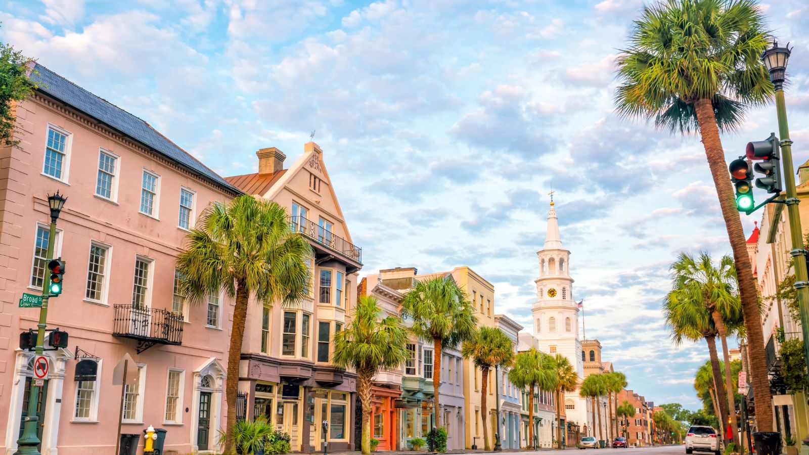 Colorful historic buildings and palm trees line a street beneath a blue sky, with a white church steeple in the background.