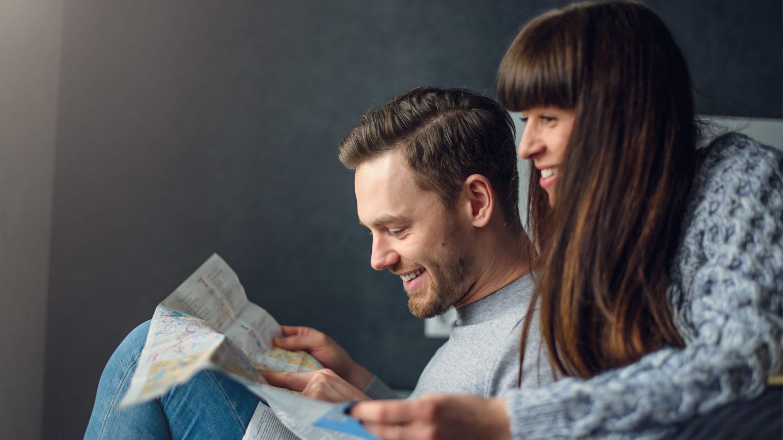 A man and woman sit close together, smiling as they look at a map and plan a trip.