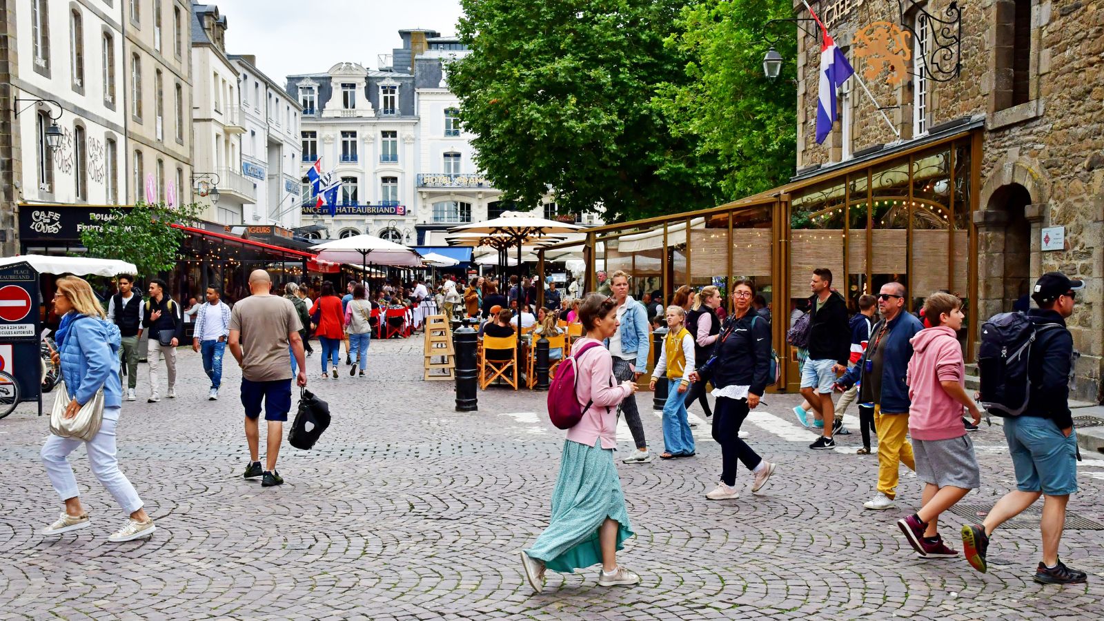 A photo of a travelers walking through a lively European street with cafés, shops, and historic buildings.
