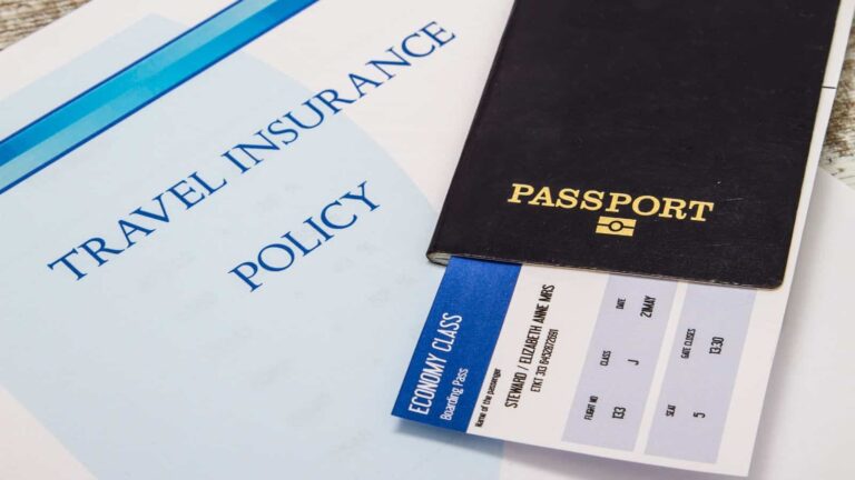 A travel insurance policy document sits beside a black passport and a blue and white economy class boarding pass, with a partially visible passenger name. Avoid common airport mistakes by ensuring all your travel essentials are in order before your journey.