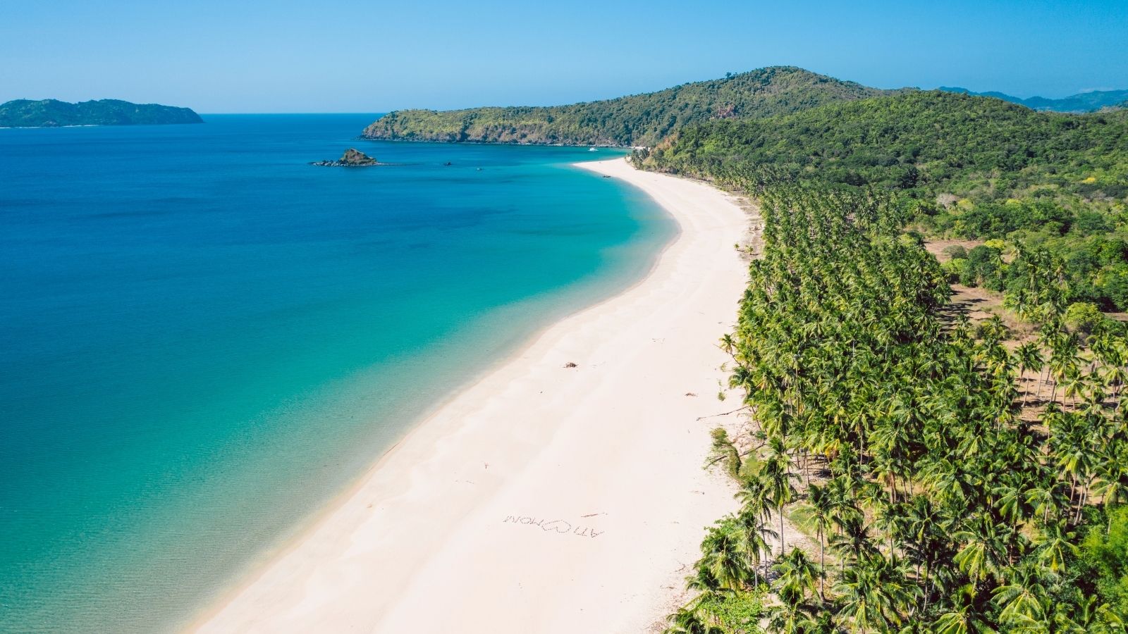 Long curved tropical beach with dense palm trees along Nacpan Beach in Palawan.