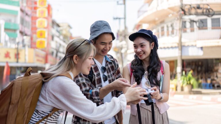 Three young adults smile at the camera on a city street, with buildings and signs in the background.