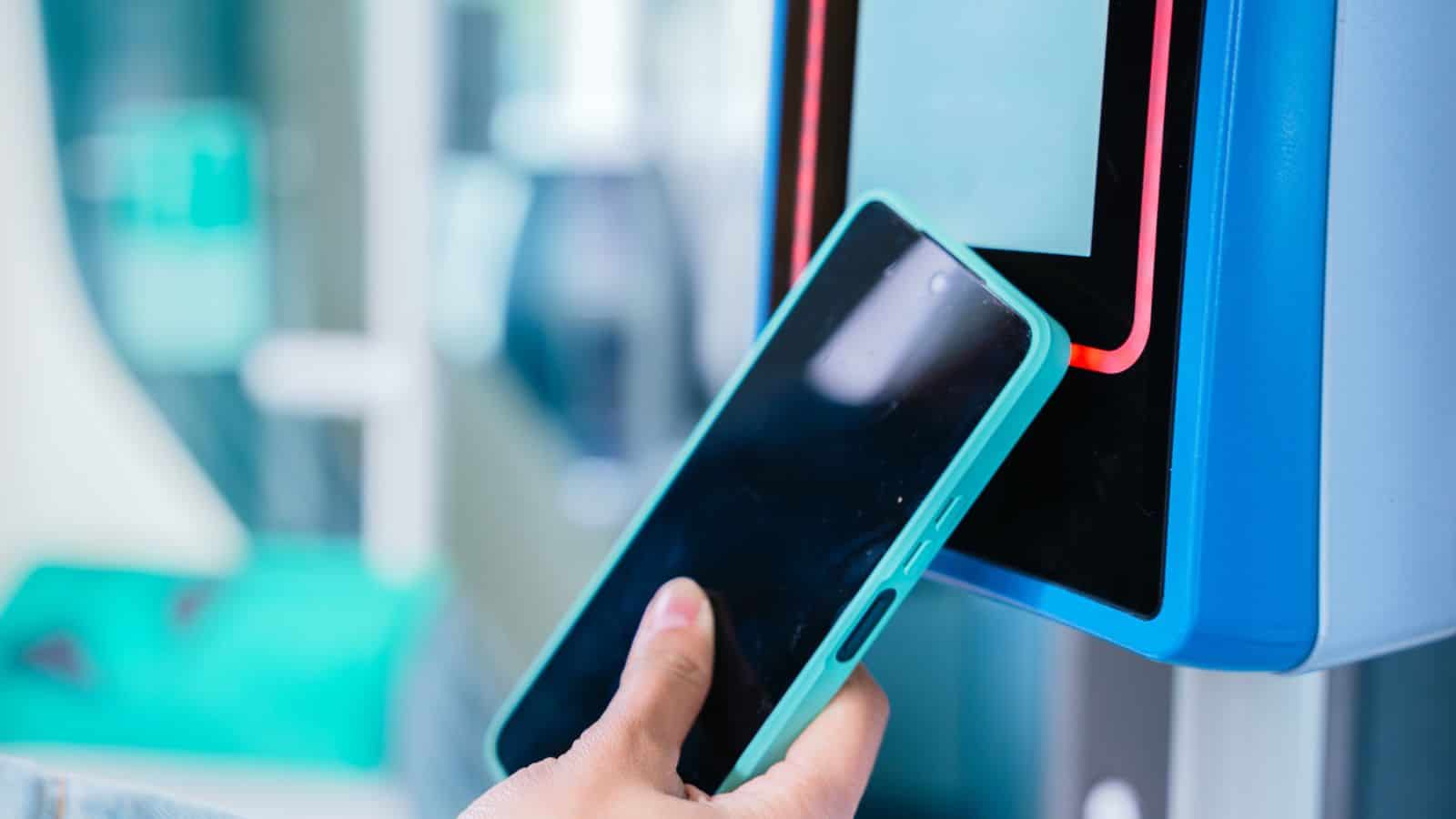 A person uses a smartphone near a card reader for contactless payment or access.