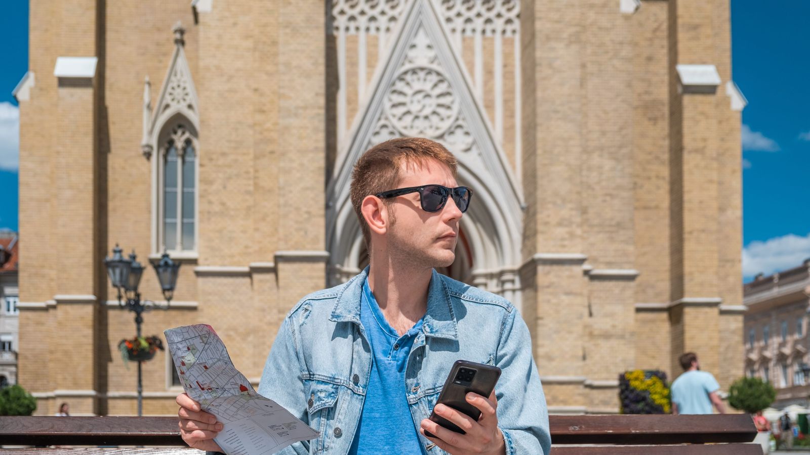 A photo of a traveler standing in city checking phone map or itinerary distracted from surroundings travel planning habit candid realistic.