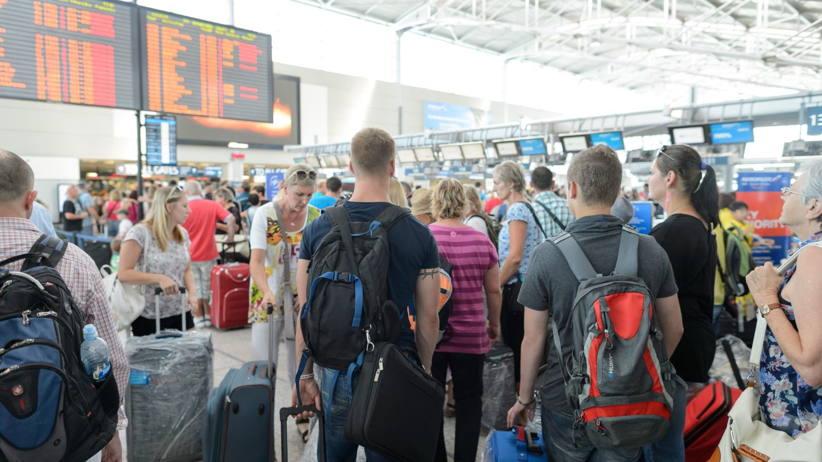 A photo of a busy airport terminal on a Friday afternoon with many travelers carrying luggage and checking departure boards.