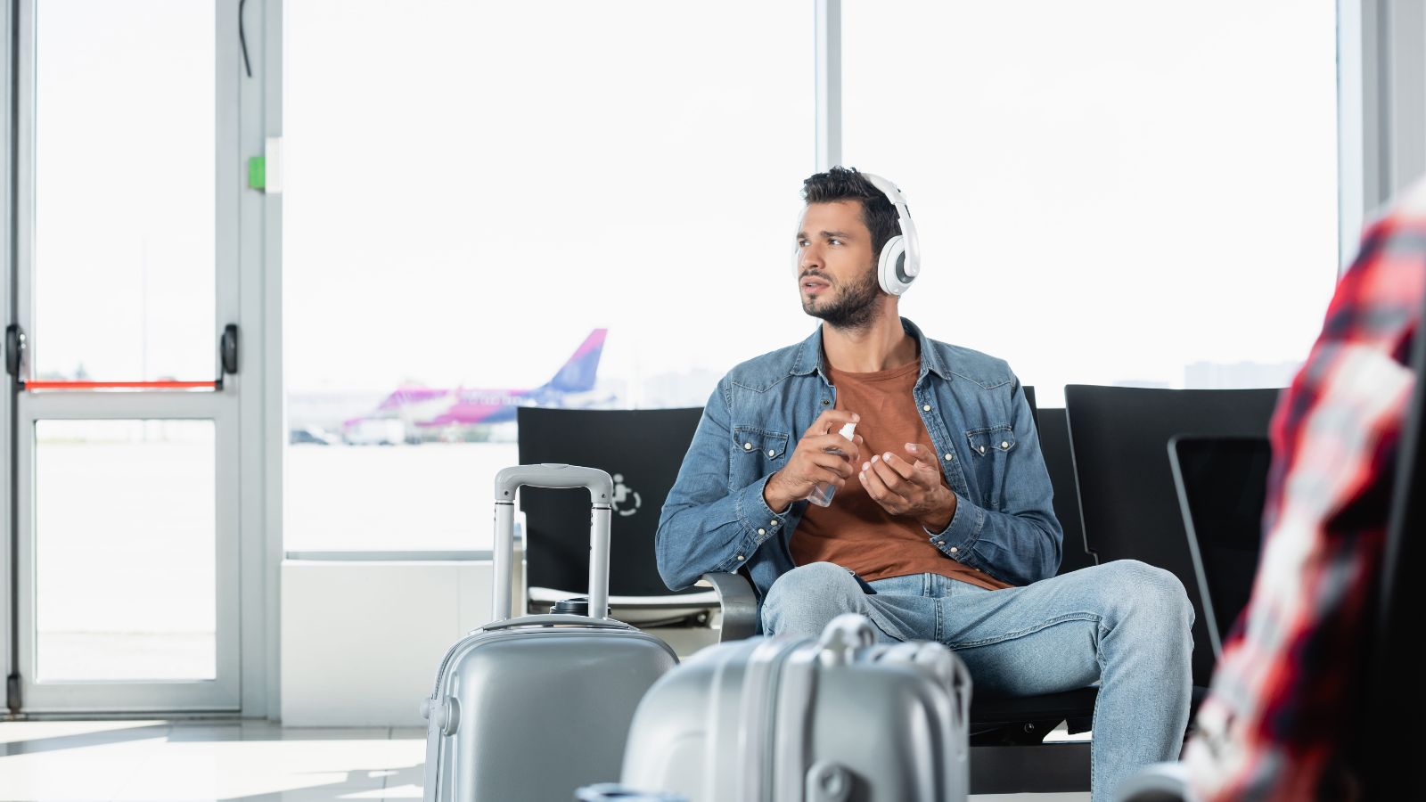 A photo of a calm traveler sitting at airport gate waiting while others line up relaxed confident travel lifestyle candid.