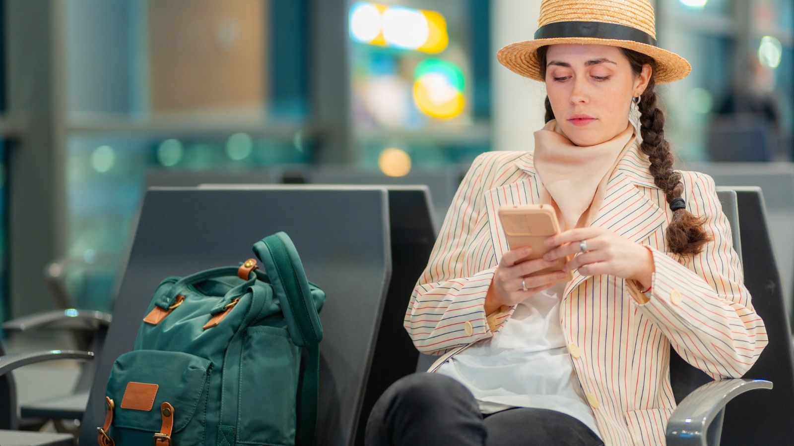 A photo of a traveler sitting at an airport terminal reviewing travel expenses on a phone while waiting for a flight.