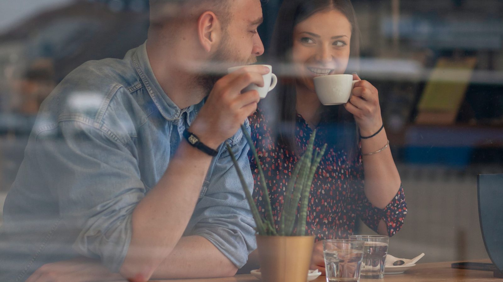 A photo of couple sitting together in a cozy café during rainy weather, smiling and enjoying coffee despite changed plans.