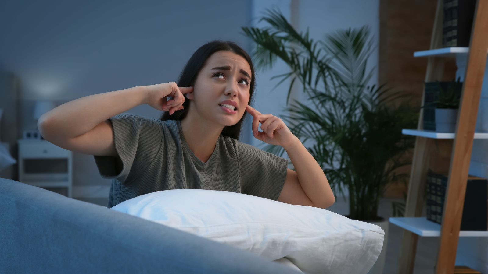 A photo of a traveler in hotel room at night unable to sleep noise disturbance covering ears or looking tired realistic candid.