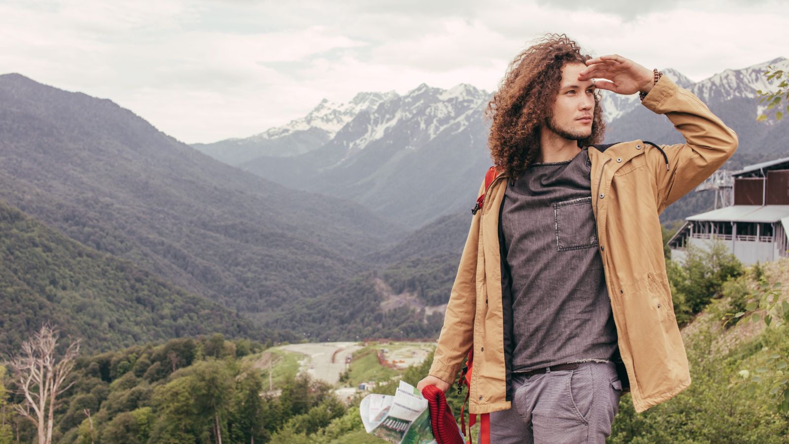 A photo of a traveler wearing city clothes standing near a Canadian mountain or forest trail looking unprepared.