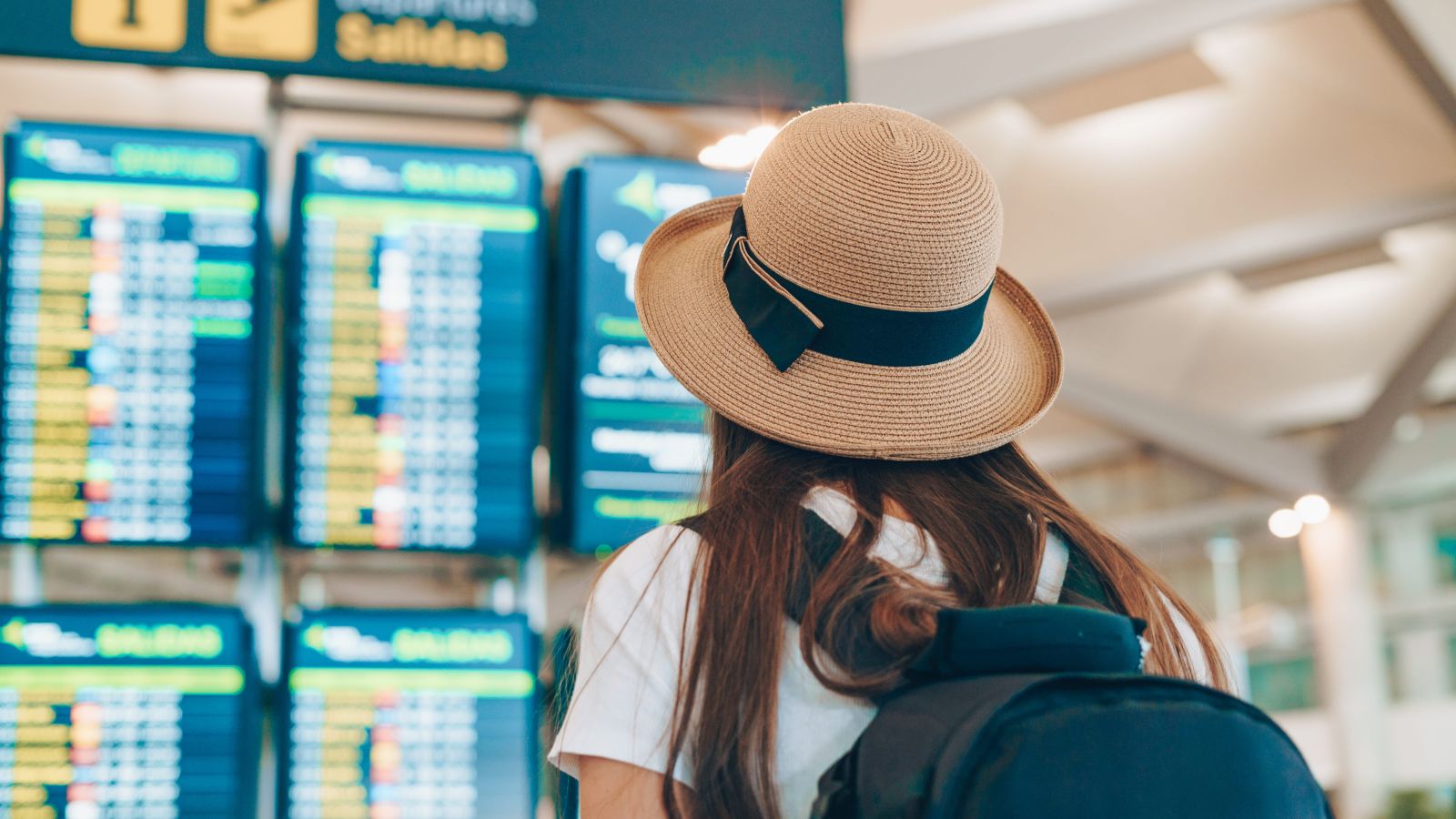 A photo of a airport departure board showing flights on different days while a traveler compares options, highlighting Tuesday and Wednesday departures.