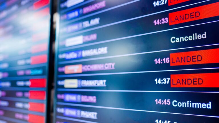 Close-up of an airport arrivals board displaying "Landed," "Cancelled," and "Confirmed" in red and white on digital screens.