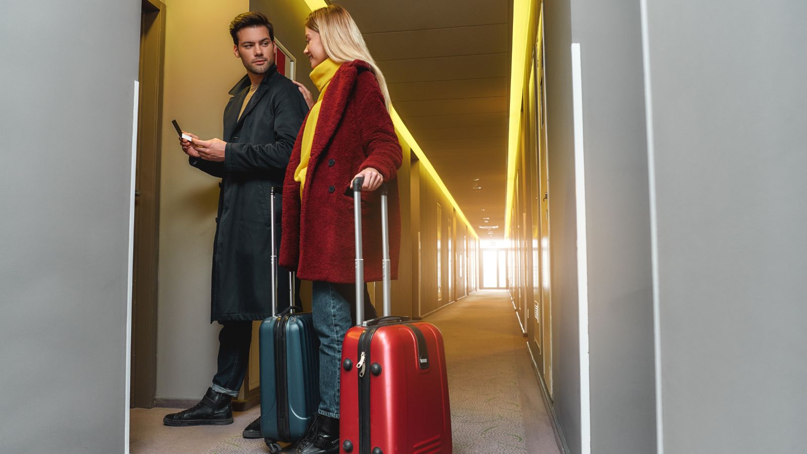 A photo of a hotel hallway with elevator and guests rolling suitcases.